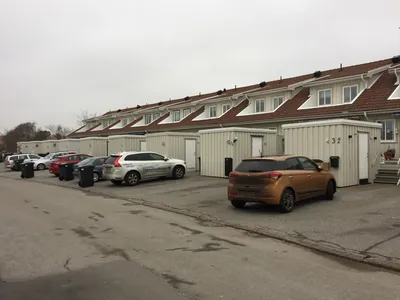 Före: radhuslänga med kvistar och bruna, bleka tak sedd från parkeringen hos BRF Gjutaren i Lysekil