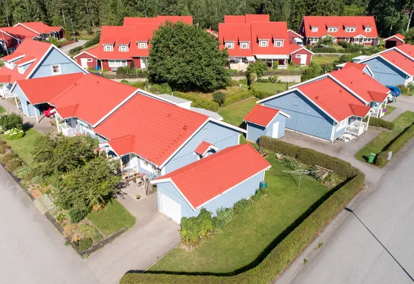 Drönarbild över villaliknande radhus med blå fasader hos BRF. Gråsparven i Nora och färdigbehandlade röda tak