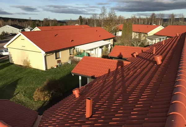 Närbild på takkam med nybehandlade orangeröda betongpannor och gula parhus hos BRF Hea i Sunne