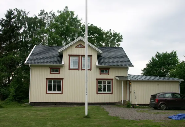 Gulvit trävilla med röda knutar och nybehandlat antracitfärgat tak, flaggstång i förgrunden