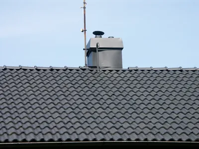 Efter: närbild på antracitpannor och murstock vid nock, med blå himmel bakom