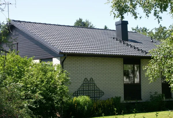 Villa med vit tegelfasad och nybehandlat tak i antracit, skorsten och buskar framför