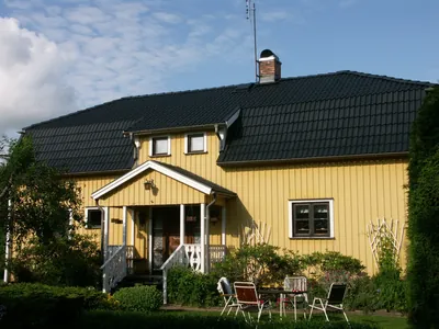 Efter: gul villa med vit farstukvist och färdigbehandlat tak i antracit, uteplats framför