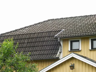 Före: närbild på urblekta, mossbelagda betongpannor vid takfoten och stuprännan