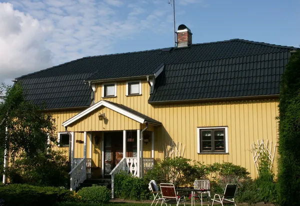 Gul trävilla med vita snickerier, farstukvist och nybehandlat tak i antracit, sedd från trädgården