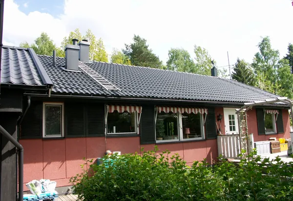 Villa med rosaröd fasad, mörka fönsterluckor och nybehandlat tak i antracit