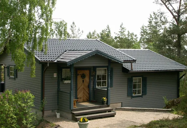 Grå trävilla i skogsmiljö med nybehandlade antracitfärgade Zanda-pannor och snidad farstukvist
