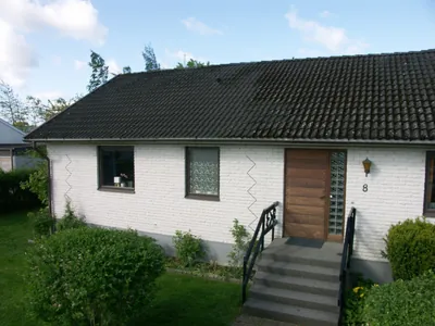 Före: vit tegelvilla med mörkt, mossigt tak på grova Zanda-pannor, sedd snett från trädgården