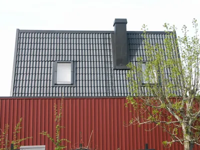 Efter: husgavel med röd fasad och färdigbehandlat tak i ljus antracit, svart skorsten