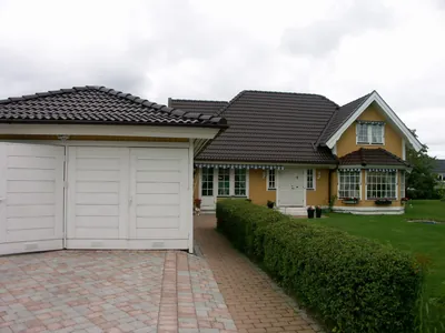 Efter: garage och gul villa med nybehandlat mörkbrunt tak, sedda från uppfarten