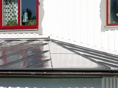 Efter: plåttak över glasverandan med färdigmålad mörkgrå yta som reflekterar omgivningen