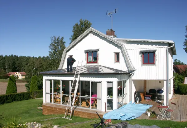 Vit villa med frontespis och glasveranda, plåttak under behandling med stege och arbetare