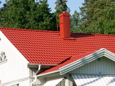 Efter: närbild på rött tak och röd skorsten ovanför vit gavelfasad och stuprör