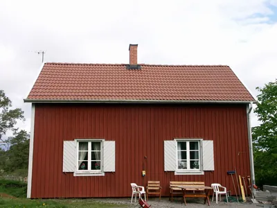 Efter: rött trähus med behandlat tak i jämn brunröd ton, stolar framför huset