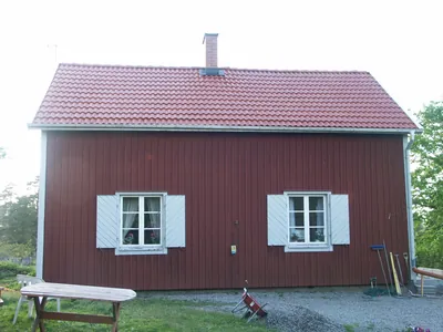 Efter: rött trähus med vita fönsterluckor och blankt, nymålat rött tak