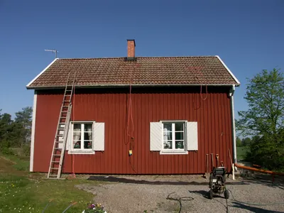 Före: rött trähus med vita fönsterluckor och mörkt, mossigt tak, stege och högtryckstvätt