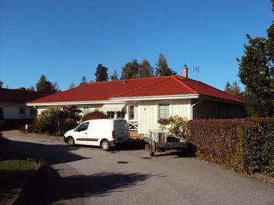 Efter: villan från gatan med färdigbehandlat tegelrött tak, vit skåpbil och släpvagn på uppfarten