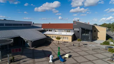 Efter: skolgården vid Lagmansgymnasiet med entré och färdigbehandlade tak mot blå himmel