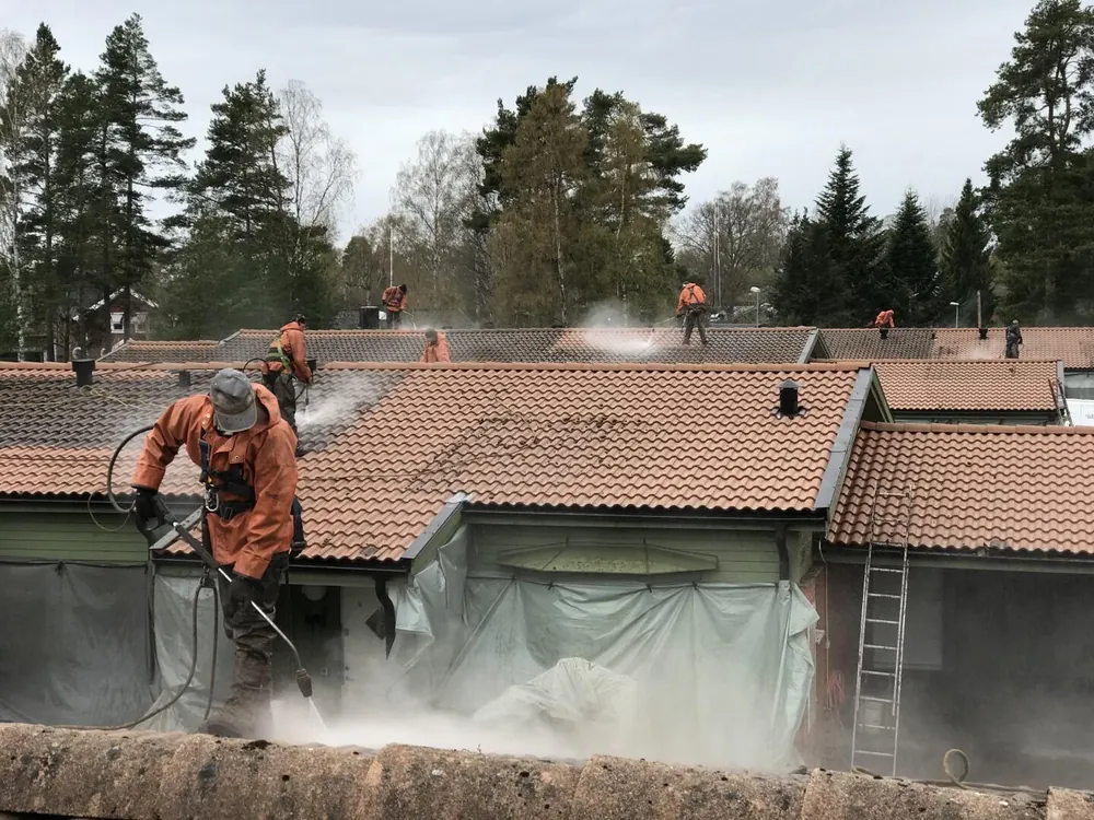 Takarbetare högtryckstvättar ett betongpannetak medan fasaden under är täckt med plast